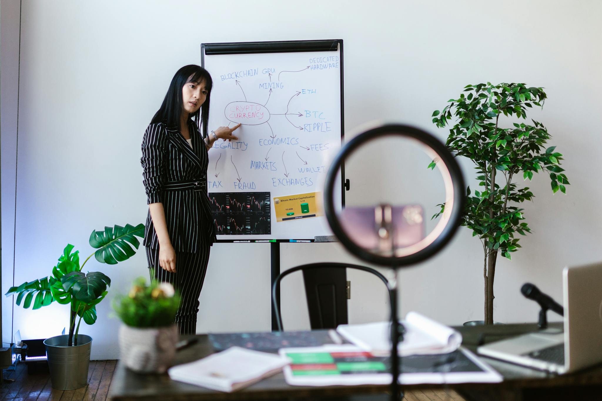Asian woman presenting cryptocurrency concepts in an office setting with a whiteboard and plants.