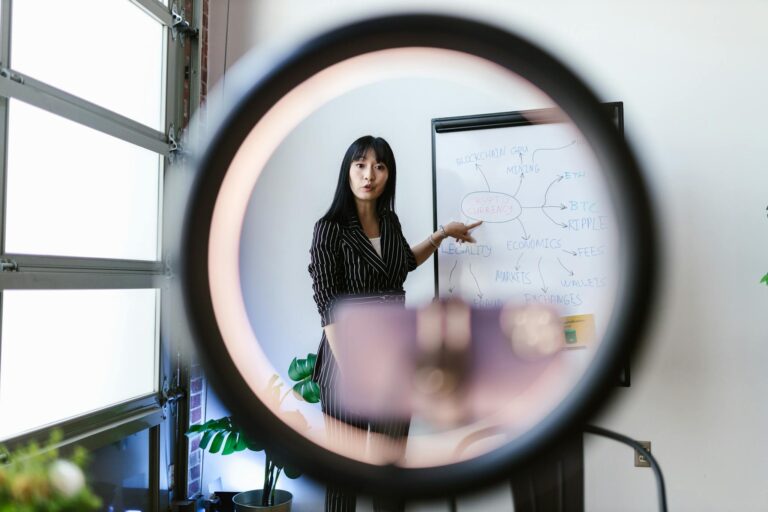 An Asian woman explaining blockchain concepts using a whiteboard, viewed through a ring light.